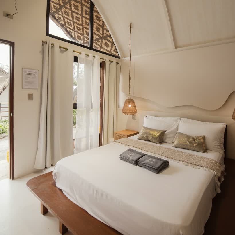 Queen bed under the tall pitched ceiling of the Beach Bungalow, the door open to the garden