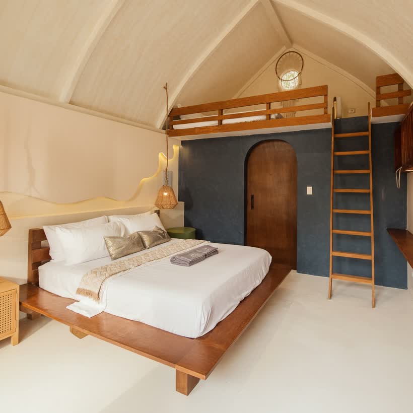 The bungalow in full: queen bed, wooden ladder to the loft and an arched door in the deep-blue wall