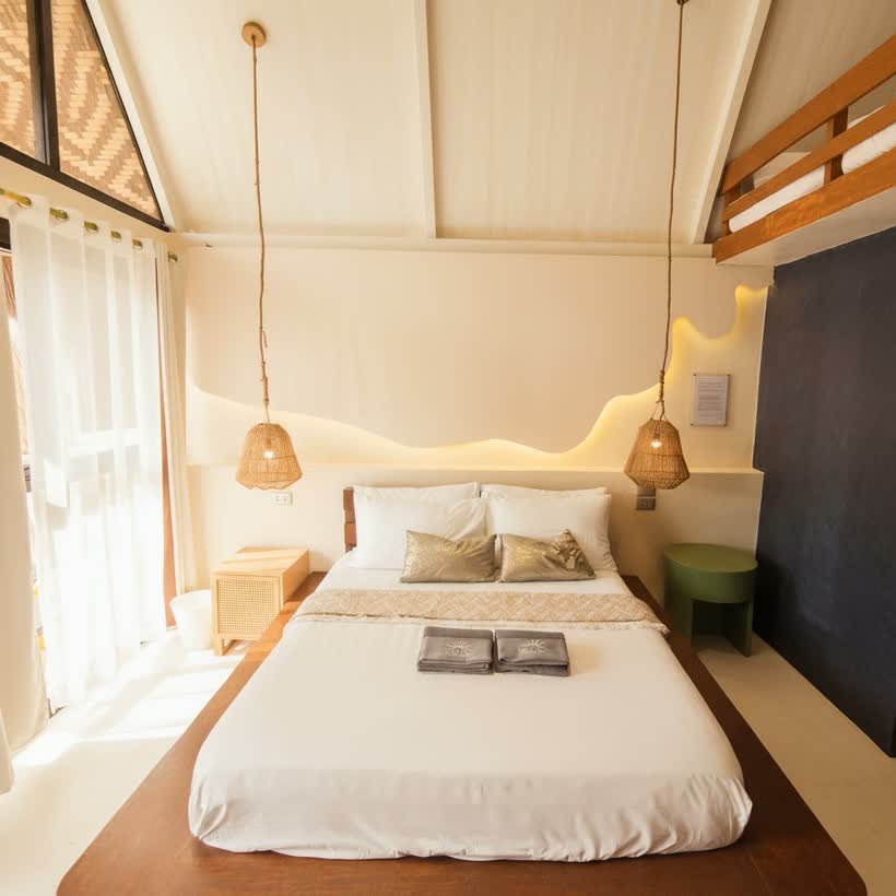 The queen bed between two hanging rattan lamps, the wave-cut headboard wall backlit